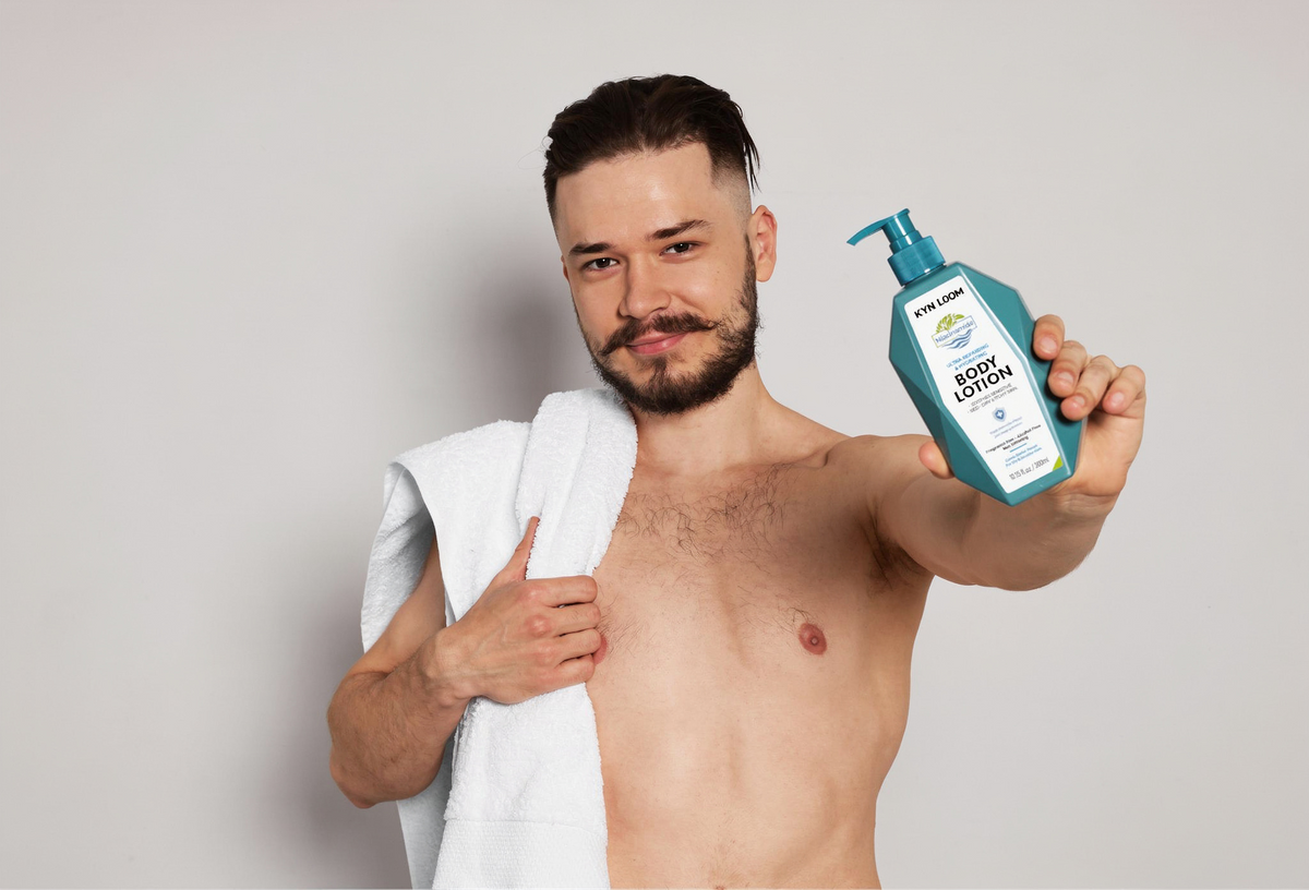 Man holding a bottle of baby lotion with a white towel on a plain background